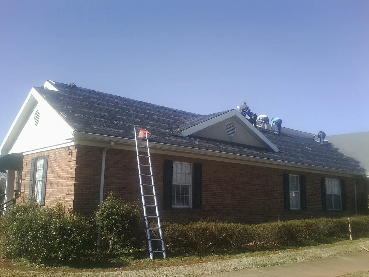 Crew tearing shingles off a brick ranch roof with a ladder set — Metal Roof Repair work by our crew in Millville