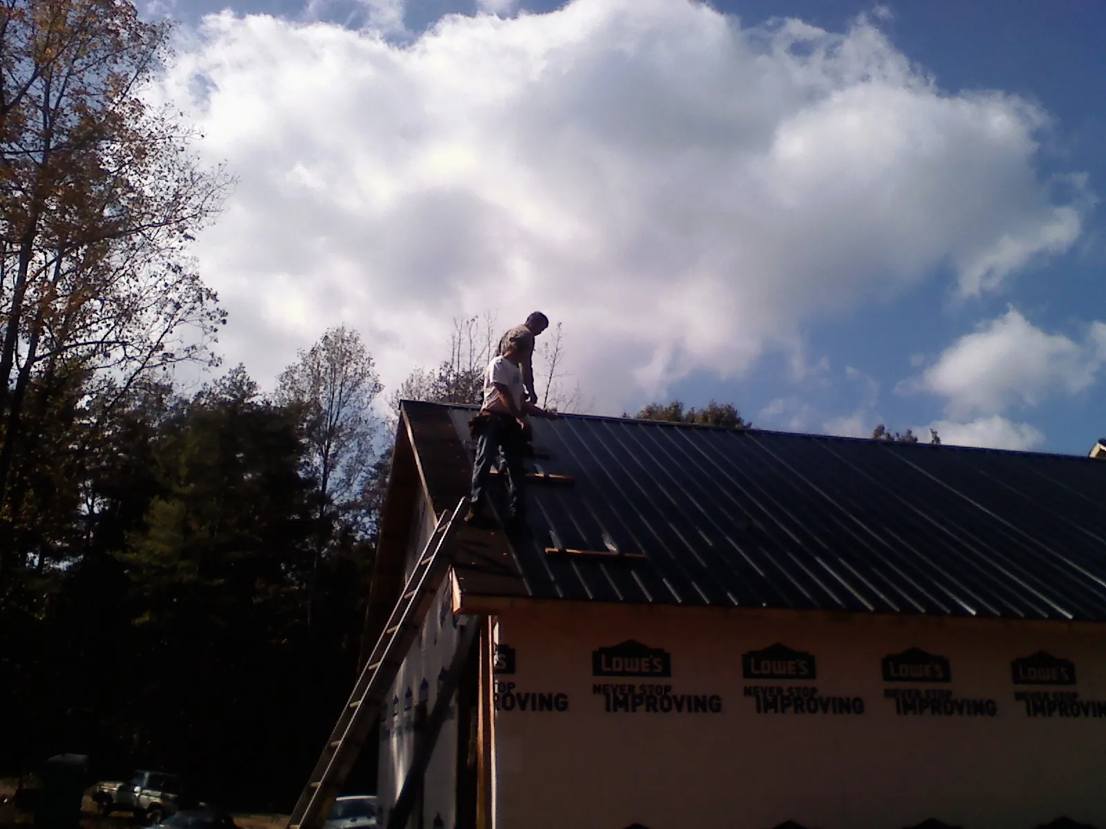 Roofer fastening dark metal panels high against a cloudy sky, from a Roof Inspection job in Millville